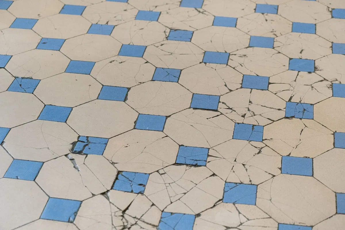 Close-up of cracked tiles featuring a blue and white geometric pattern, highlighting the need for floor restoration.